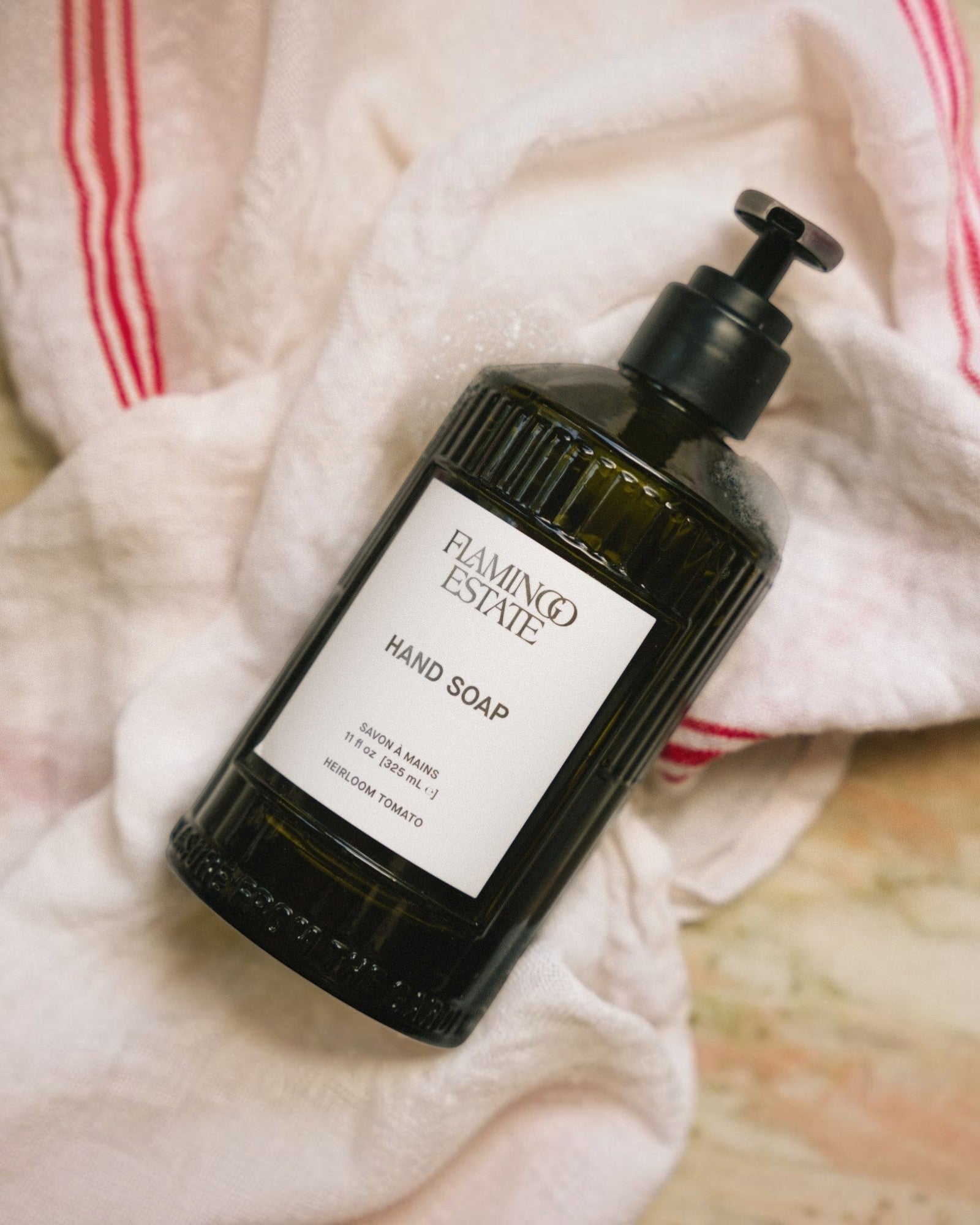JONES + CO Heirloom Tomato hand soap in a dark green fluted glass bottle with a pump dispenser on a linen cloth.