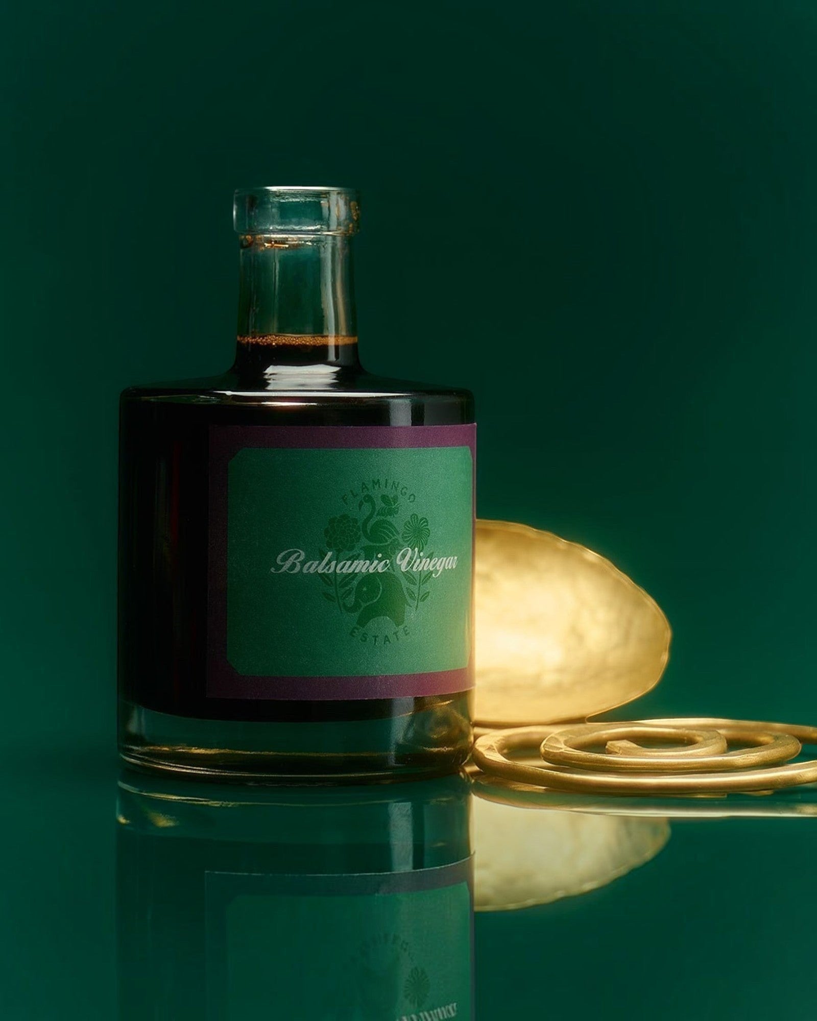 JONES + CO organic balsamic vinegar in a glass bottle with a green label, set against a dark green reflective surface.