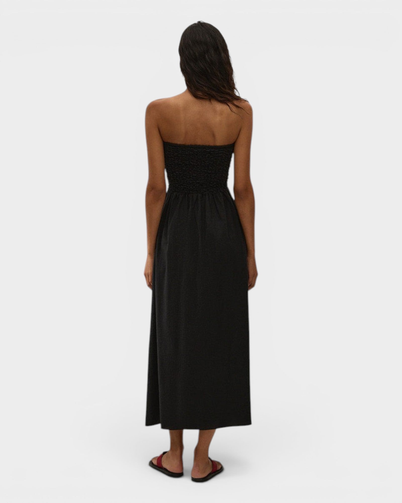 JONES + CO Orla black strapless midi dress in stretch-cotton with a smocked bodice, worn by a model against a wall.
