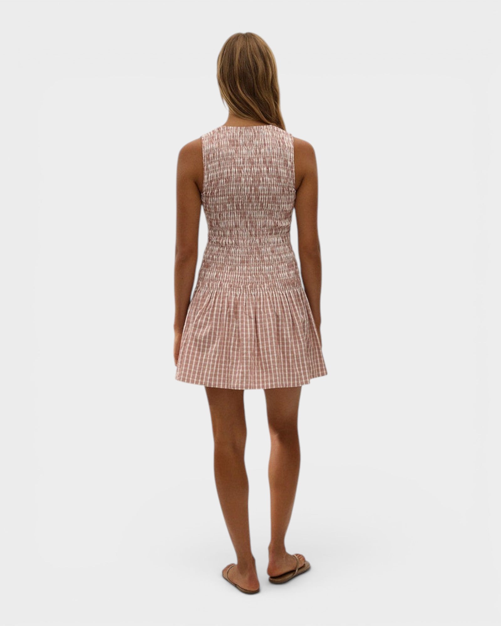Back view of a model wearing a JONES + CO Palomar mini dress in cinnamon and white check cotton with shirred bodice.