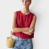 Model wearing a JONES + CO sleeveless Pompeian red linen top with button front and boxy fit, paired with blue jeans.