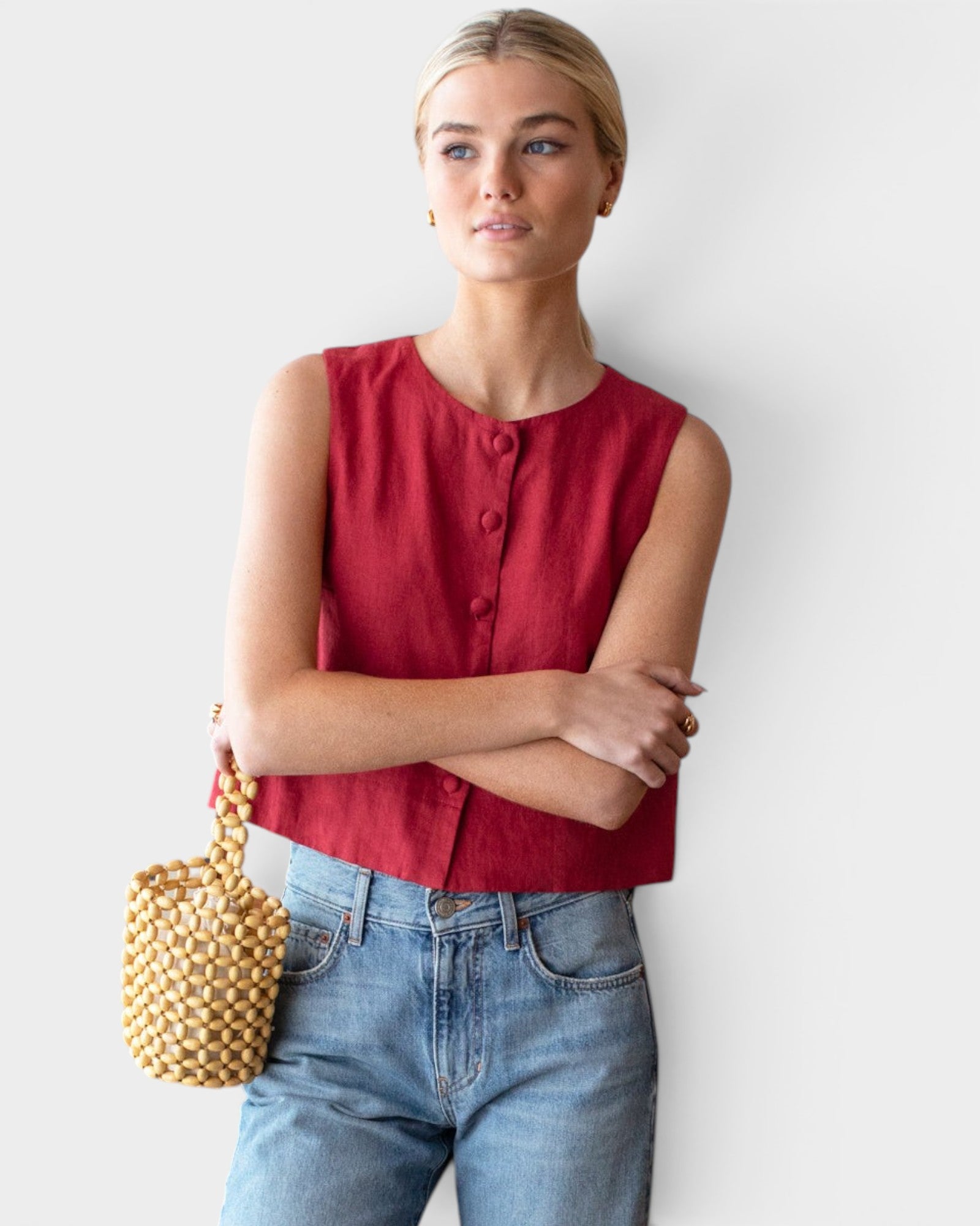 Model wearing a JONES + CO sleeveless Pompeian red linen top with button front and boxy fit, paired with blue jeans.