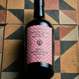 JONES + CO Spicy Extra Virgin Olive Oil in a dark glass bottle with a pink checkered label on a geometric tile floor.