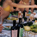 JONES + CO Spicy Extra Virgin Olive Oil in a dark glass bottle with a pink checkered label on a summer dining table.