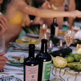 JONES + CO Spicy Extra Virgin Olive Oil in a dark glass bottle with a pink checkered label on a summer dining table.