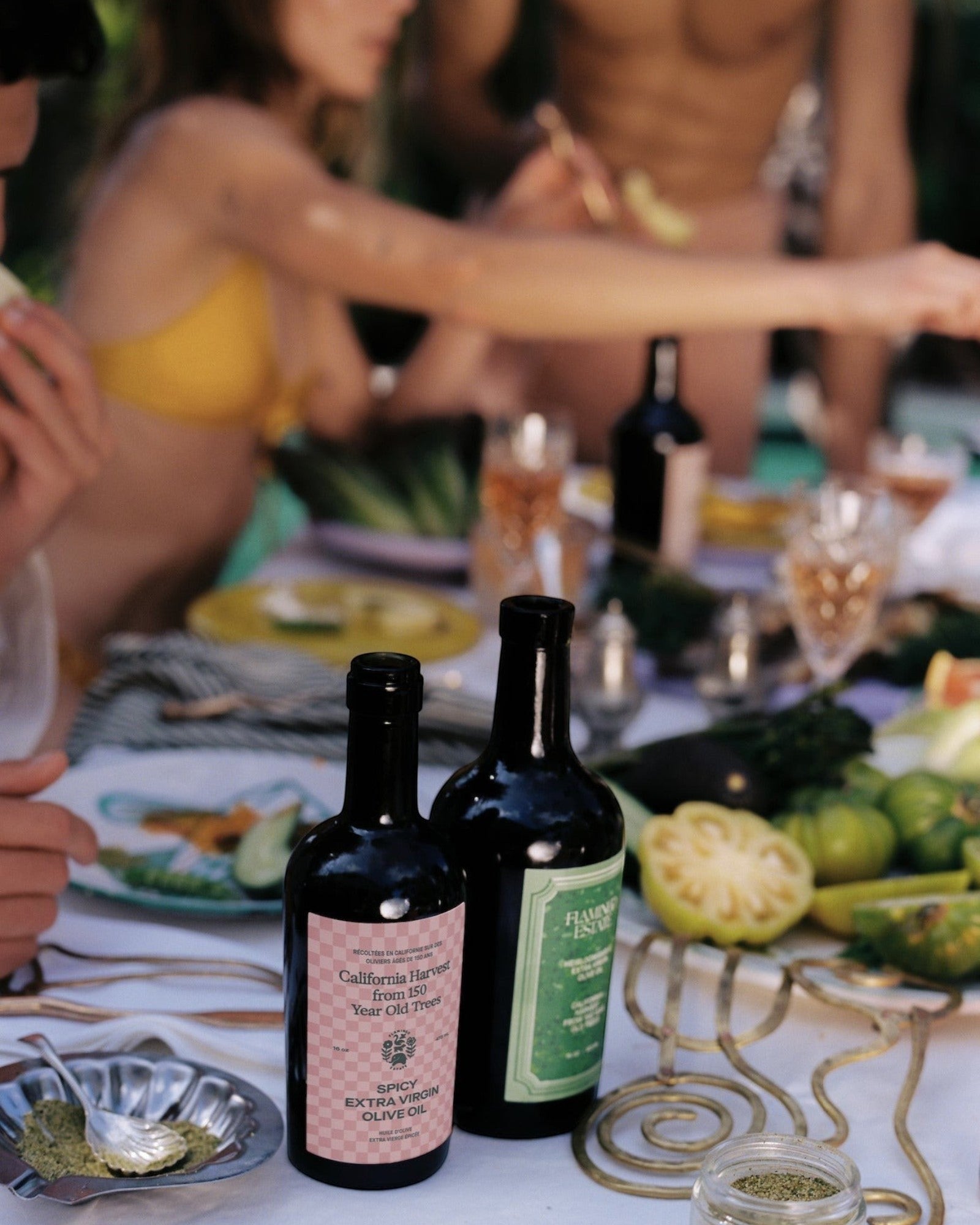 JONES + CO Spicy Extra Virgin Olive Oil in a dark glass bottle with a pink checkered label on a summer dining table.