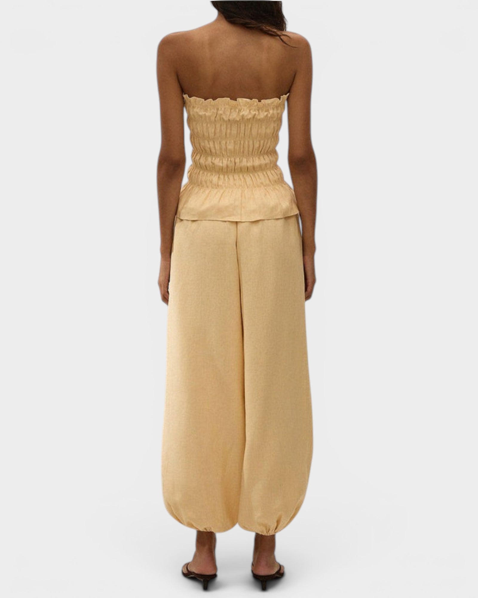Model wearing JONES + CO daffodil yellow strapless linen top with shirred bodice and peplum hem from behind.