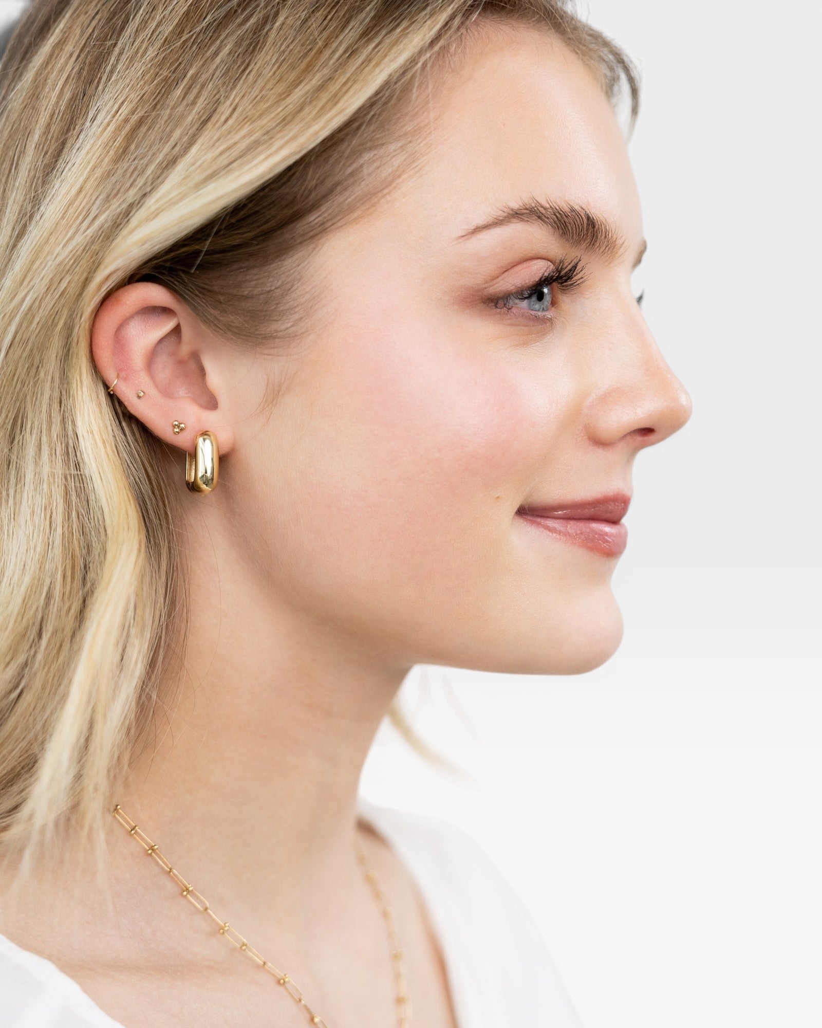 JONES + CO 14K gold chunky square tube hoop earrings worn by a blonde woman.