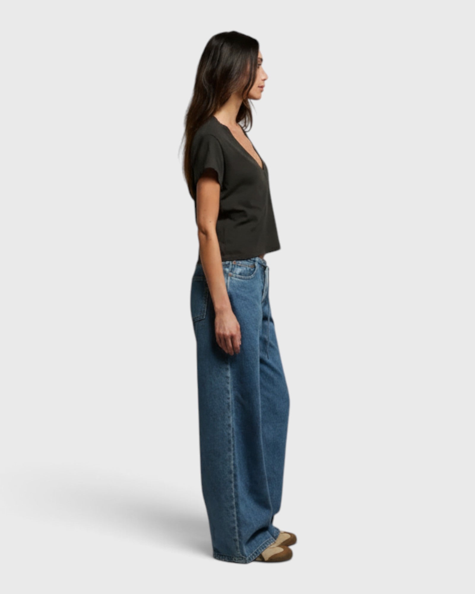 JONES + CO Alanis V-neck tee in vintage black recycled cotton, worn by a model in profile with wide-leg blue jeans.