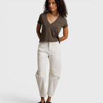Model wearing a JONES + CO dark olive recycled cotton Alanis V-neck tee with a relaxed cropped fit and white trousers.