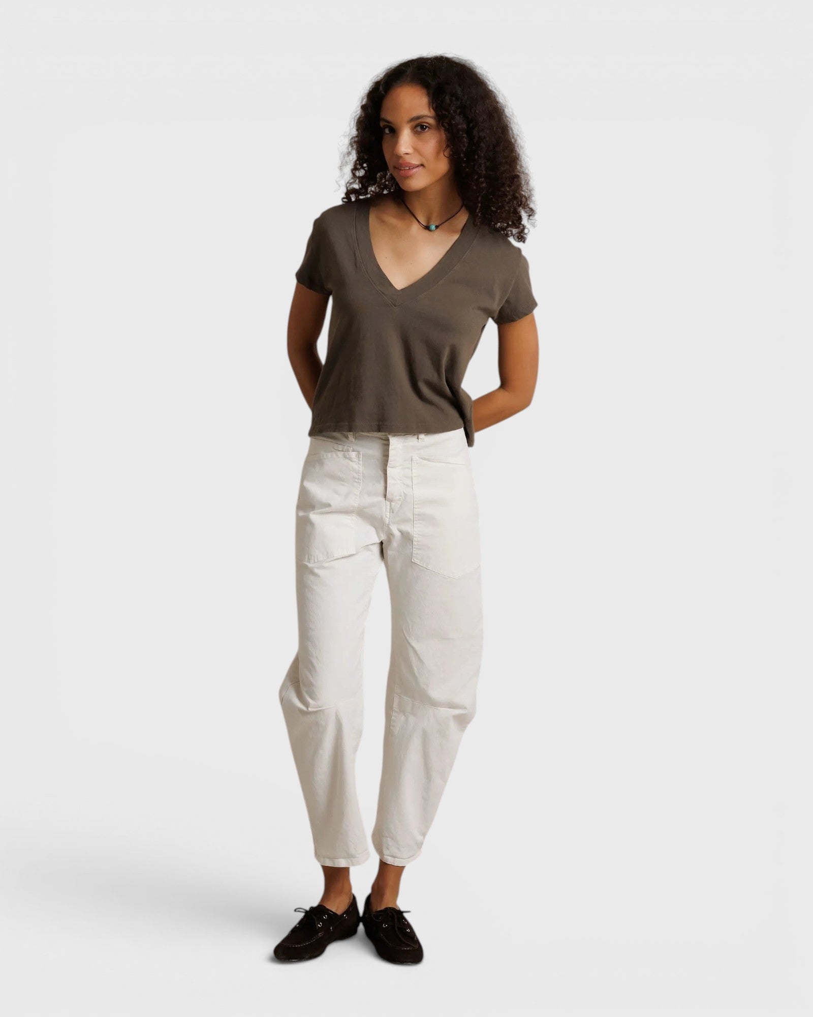 Model wearing a JONES + CO dark olive recycled cotton Alanis V-neck tee with a relaxed cropped fit and white trousers.