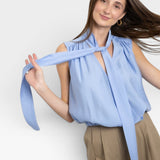 JONES + CO Amara blue sleeveless blouse with tie neck detail and gathered elastic hem. Model wears tan wide-leg pants.