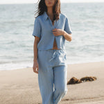 JONES + CO Anais linen shirt in baby blue, featuring a button-down front and short sleeves. Model on beach.