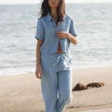 JONES + CO Anais linen shirt in baby blue, featuring a button-down front and short sleeves. Model on beach.