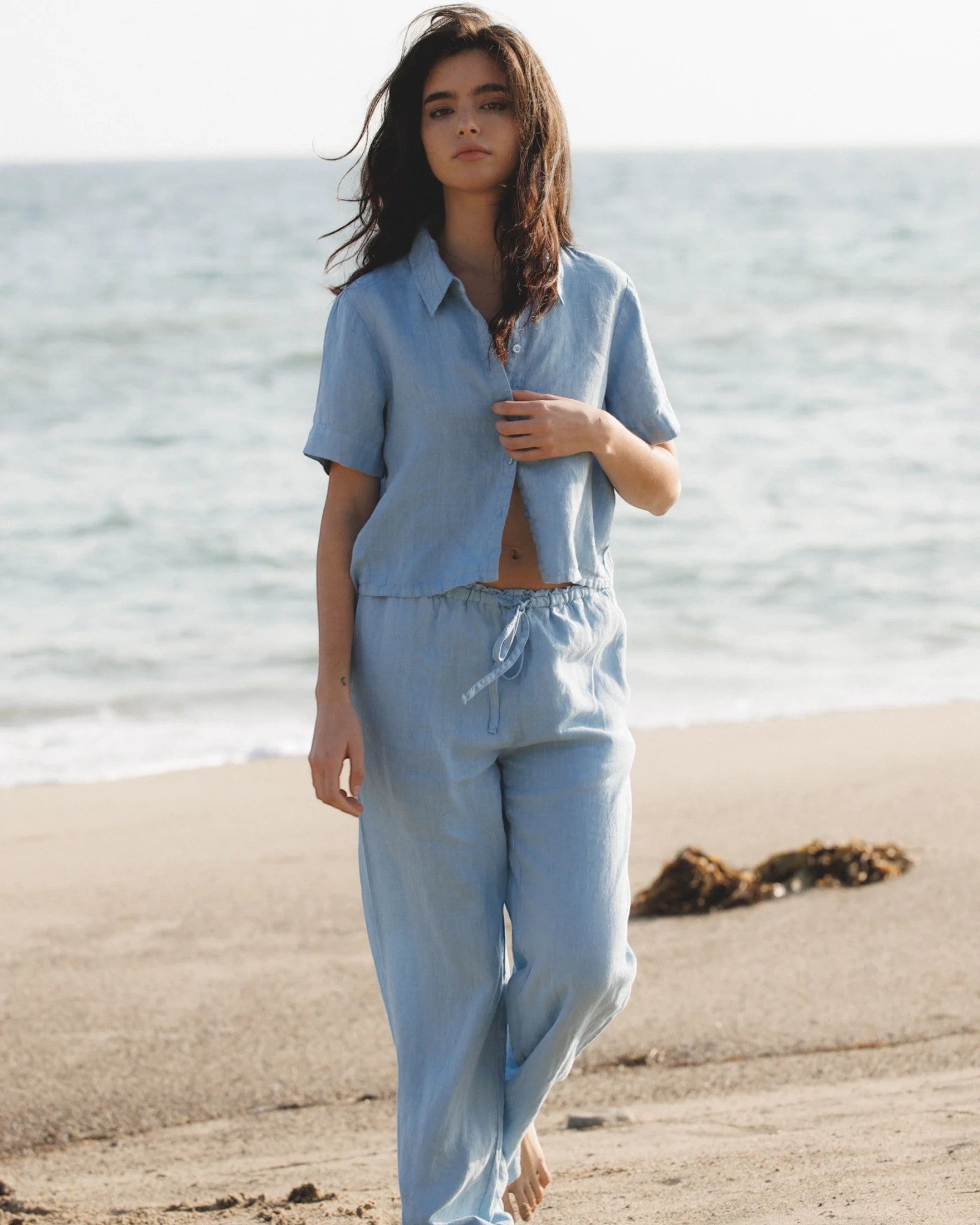 JONES + CO Anais linen shirt in baby blue, featuring a button-down front and short sleeves. Model on beach.