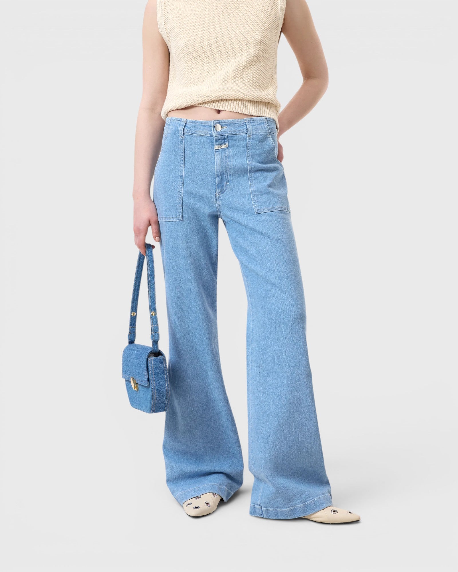 JONES + CO Aria flared jeans in light blue stretch denim with patch pockets and high waist worn with a matching bag.