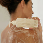 JONES + CO Awaken Body Wash bottle with botanical citrus scent, used by a woman in the shower.