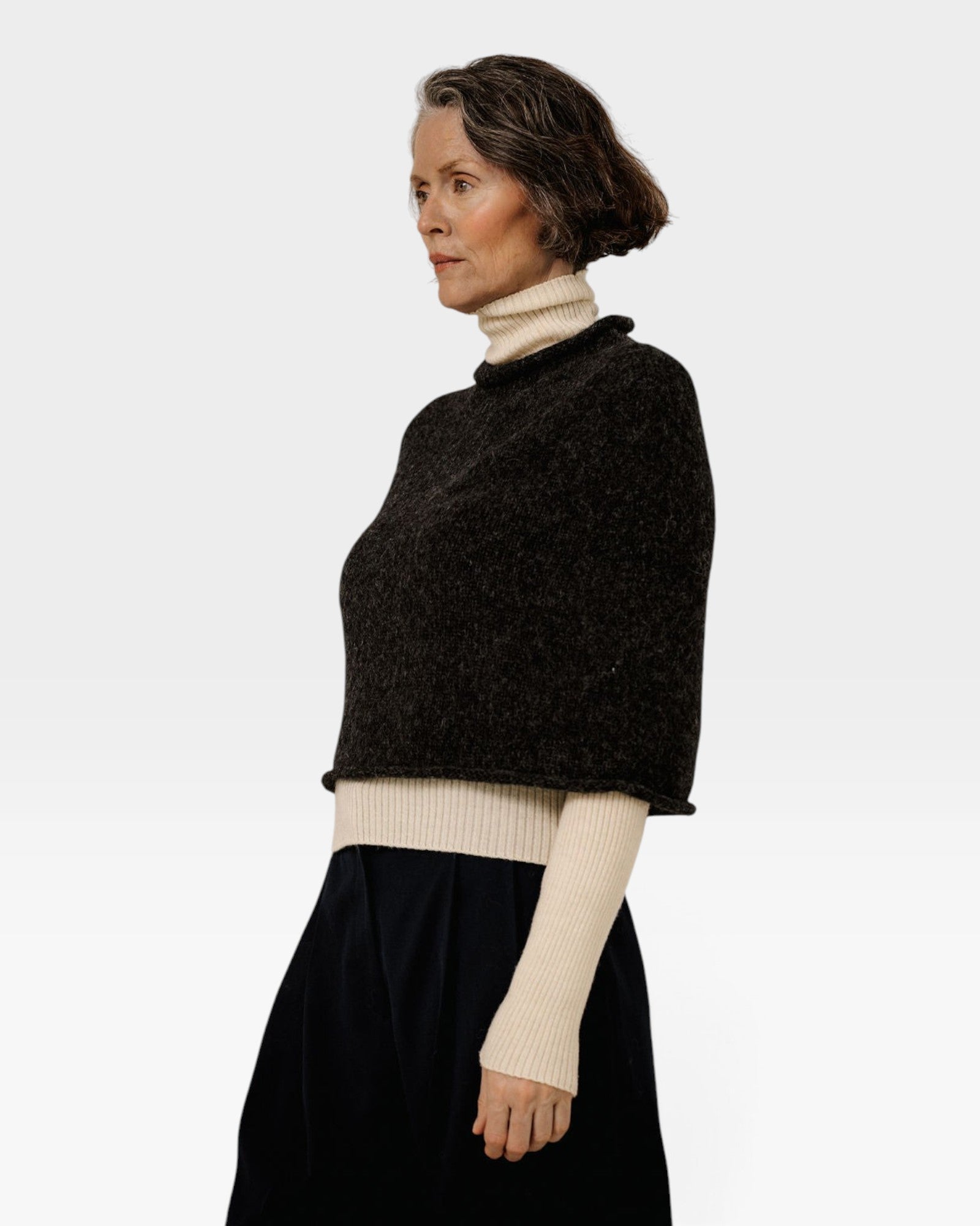 JONES + CO seamless basalt alpaca-blend poncho worn over a cream turtleneck sweater by a woman in profile view