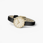 JONES + CO Beverly watch with a gold case, minimalist cream dial, and black leather strap on a white background.