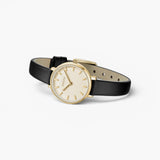 JONES + CO Beverly watch with a gold case, minimalist cream dial, and black leather strap on a white background.