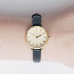JONES + CO Beverly watch featuring a minimalist gold case and black leather strap worn on a wrist.