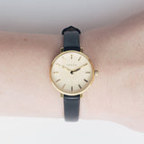 JONES + CO Beverly watch featuring a minimalist gold case and black leather strap worn on a wrist.
