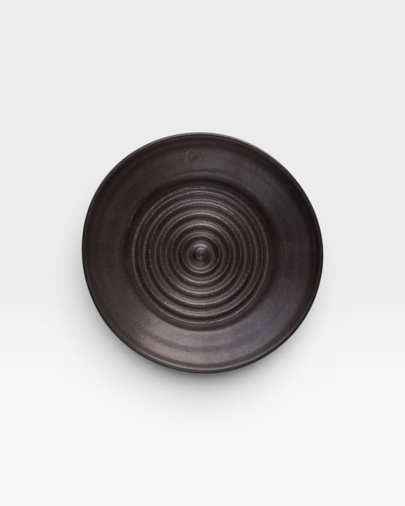 JONES + CO black ceramic garlic grater plate with a circular ridged center for grating garlic and herbs.