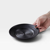 JONES + CO black ceramic garlic grater plate with raised circular ridges for grating garlic and herbs.