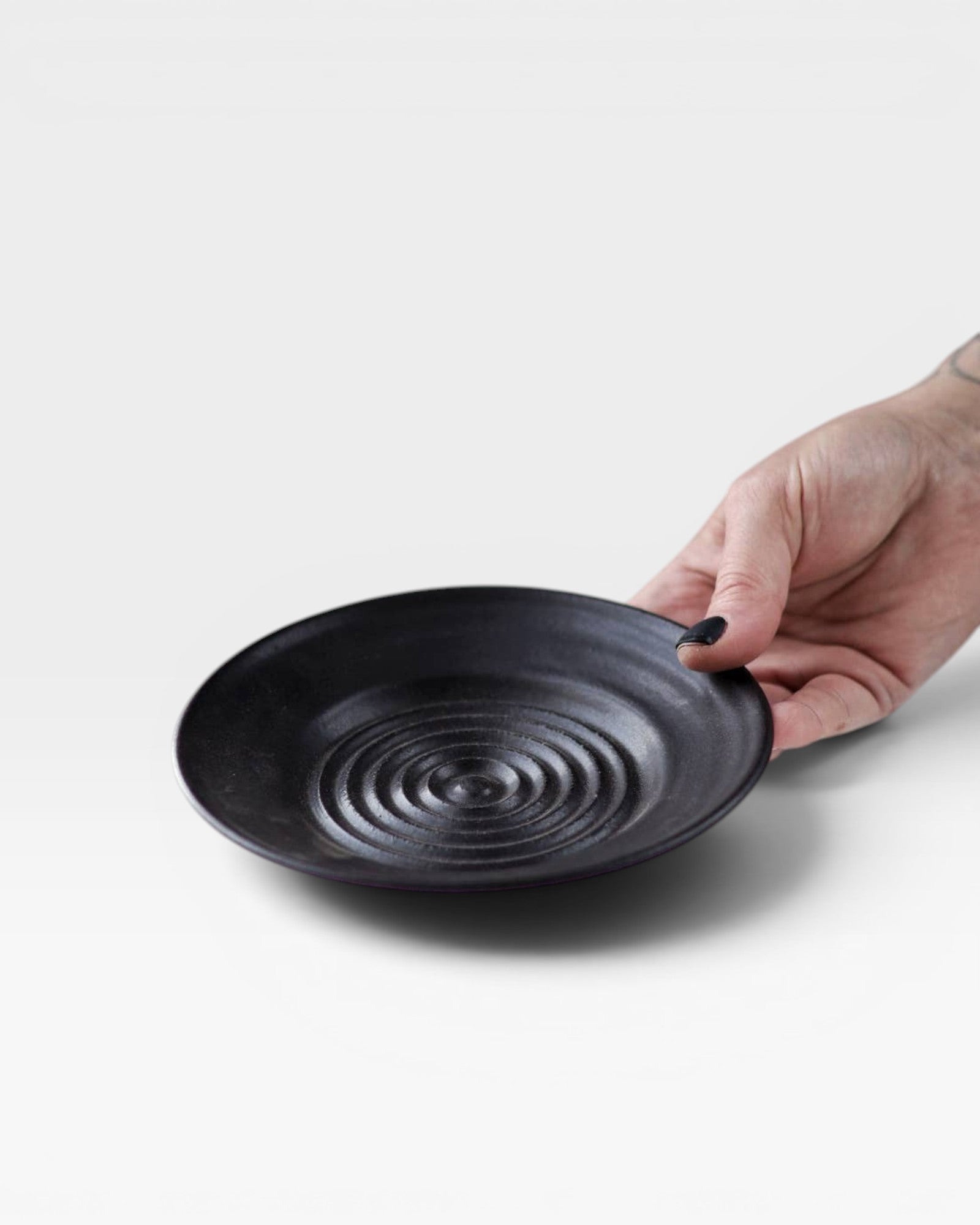 JONES + CO black ceramic garlic grater plate with raised circular ridges for grating garlic and herbs.