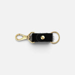 JONES + CO black cowhide keychain with gold-tone metal clasp and ring hardware on a white background.