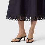 JONES + CO black midi skirt featuring intricate cut-out embroidery along the flared hem, worn with black heeled sandals