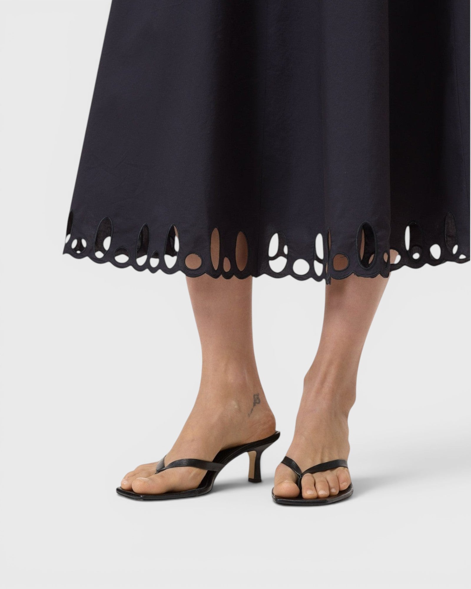 JONES + CO black midi skirt featuring intricate cut-out embroidery along the flared hem, worn with black heeled sandals
