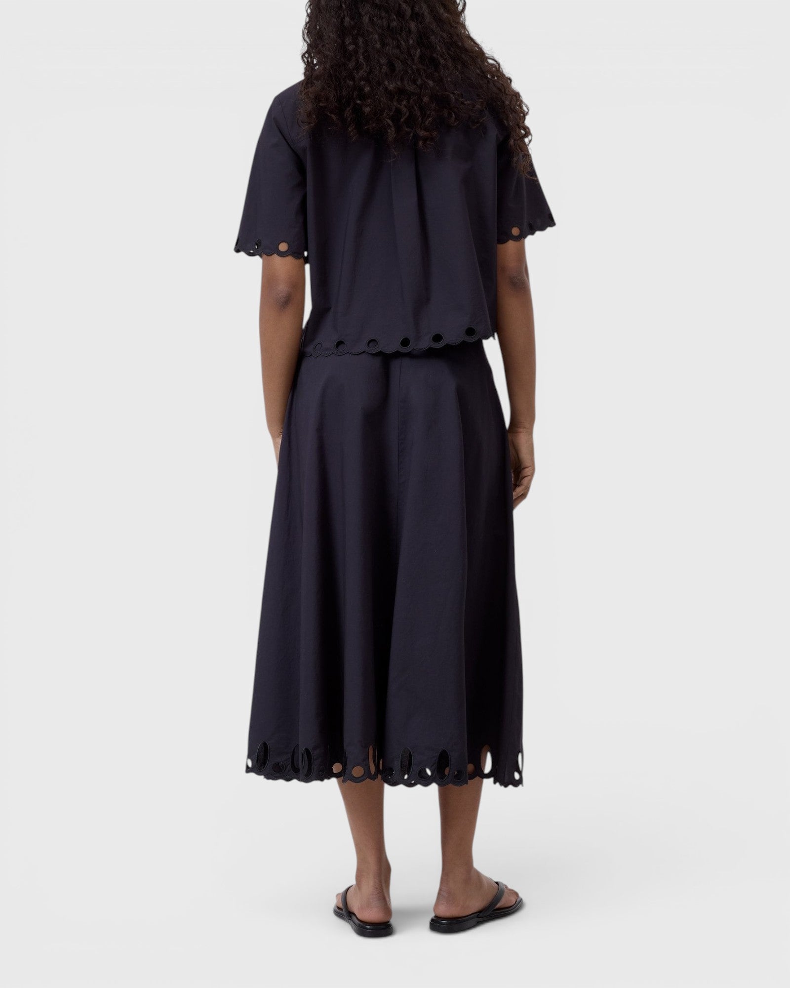 JONES + CO black cotton poplin short sleeve shirt with embroidered cut-out hem, worn with matching midi skirt.