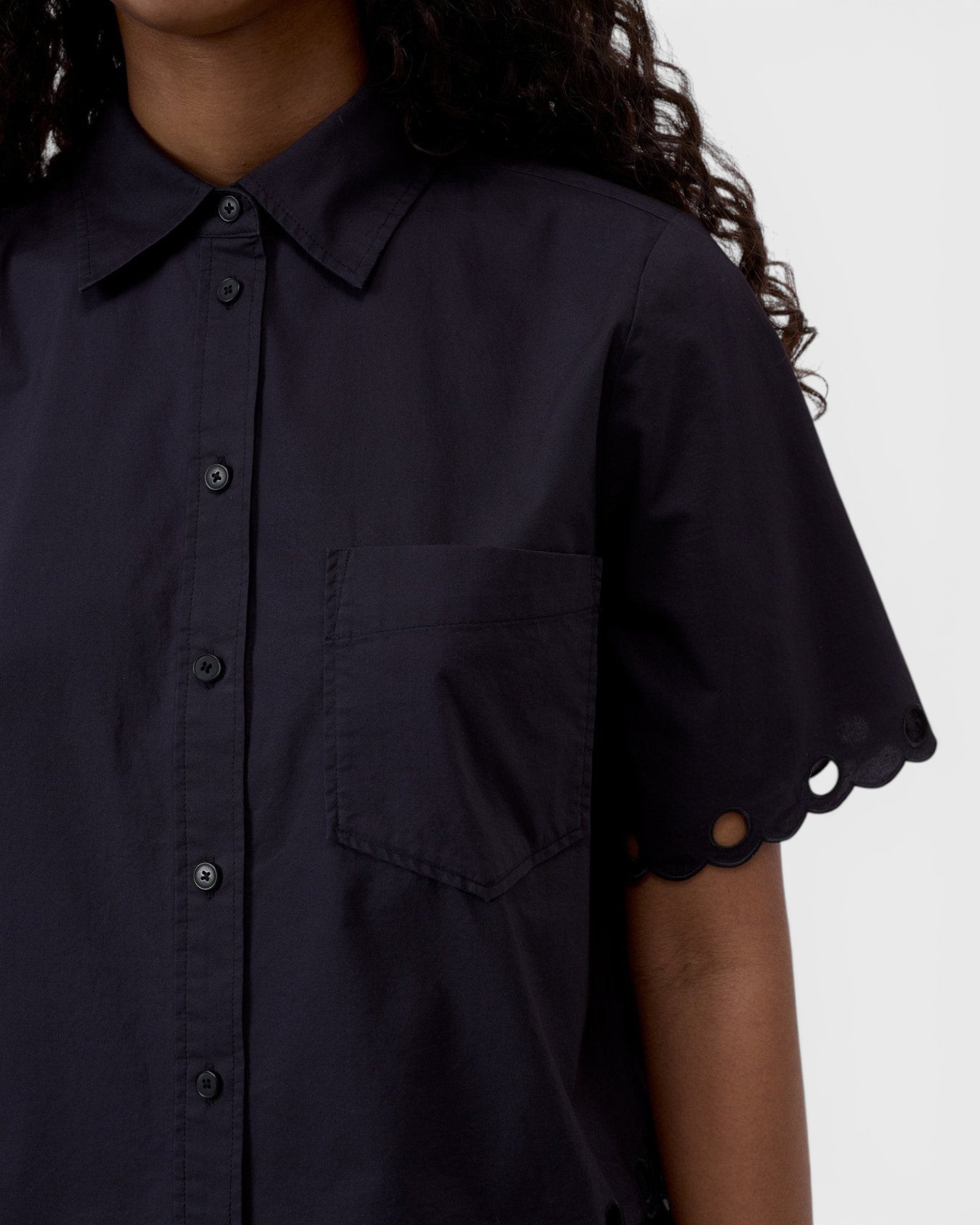 JONES + CO black cotton poplin short sleeve shirt with a pointed collar, button placket, and scalloped sleeve detail.