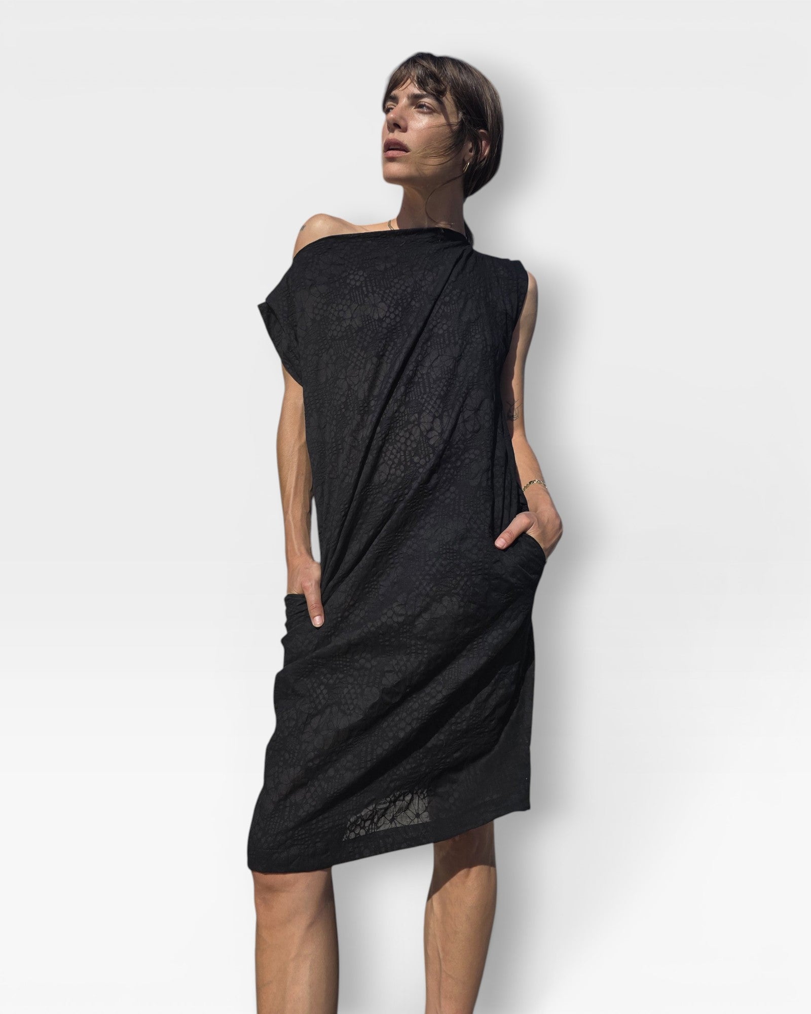 Model wearing a JONES + CO black embossed floral seersucker shift dress with an off-shoulder neckline and pockets.