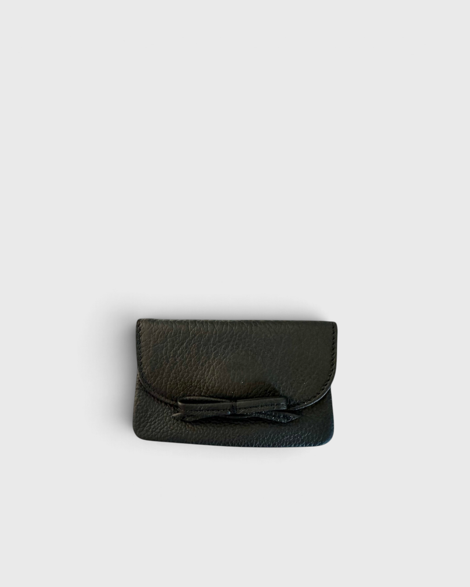 JONES + CO black leather petite card case featuring a charming knotted bow detail and slim magnetic flap closure.