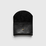 JONES + CO black leather cardholder with a rounded flap and gold snap button closure on a light grey background.