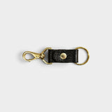 JONES + CO black leather keychain with a gold-tone metal clasp and ring on a light grey background.