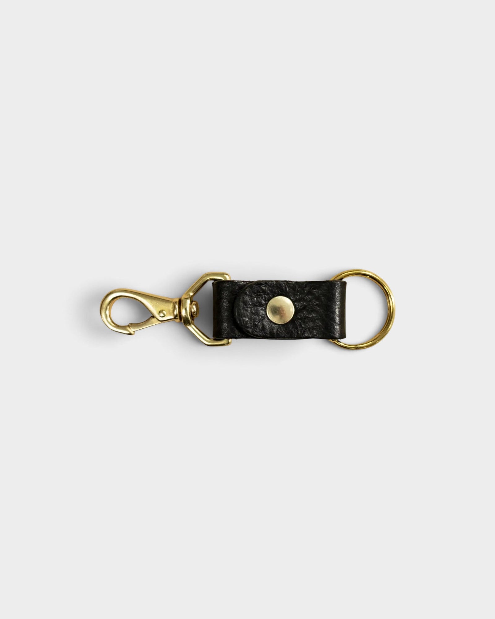 JONES + CO black leather keychain with a gold-tone metal clasp and ring on a light grey background.