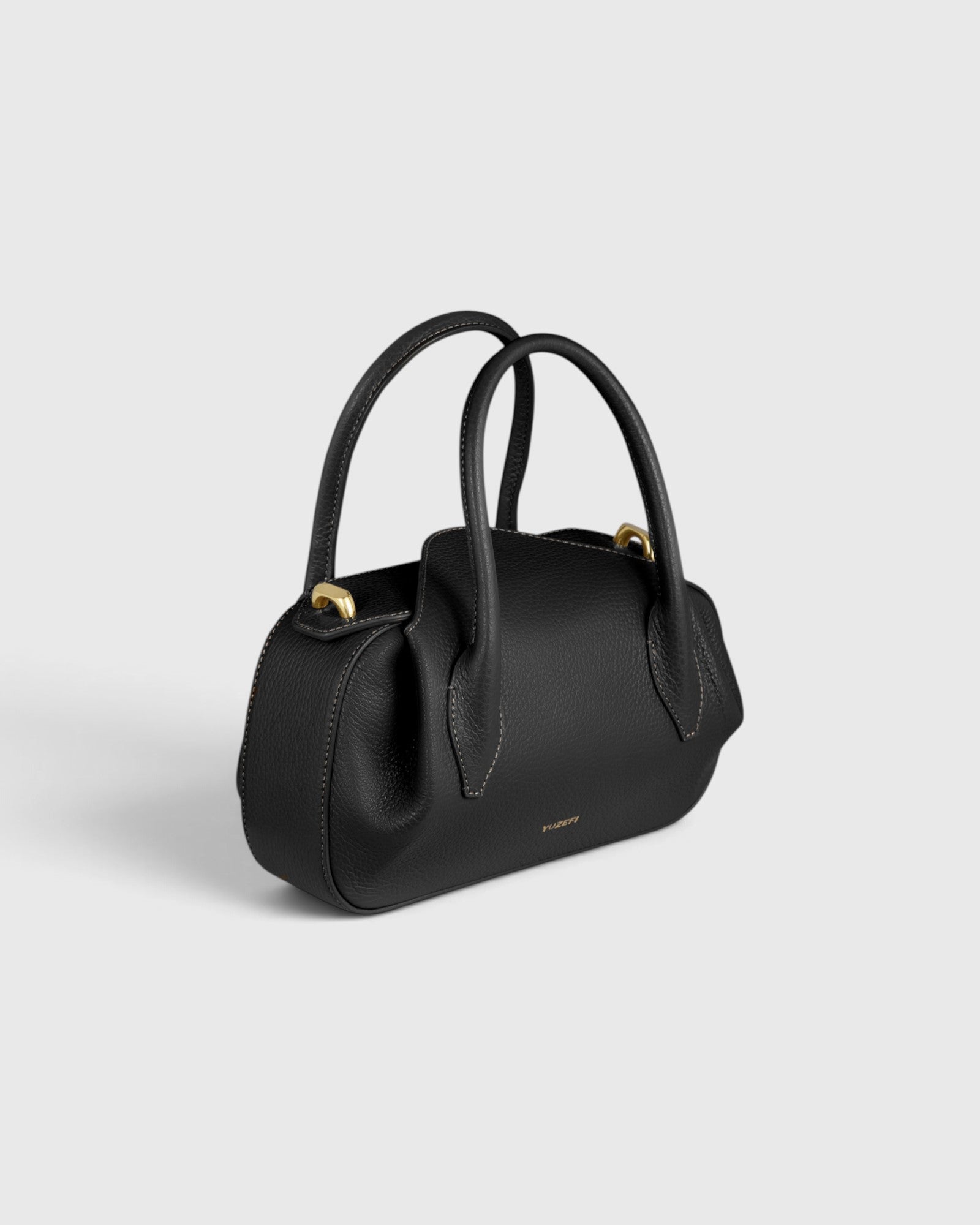 JONES + CO Oyster mini duffle bag in black pebble grained leather with gold-tone hardware and structured top handles.