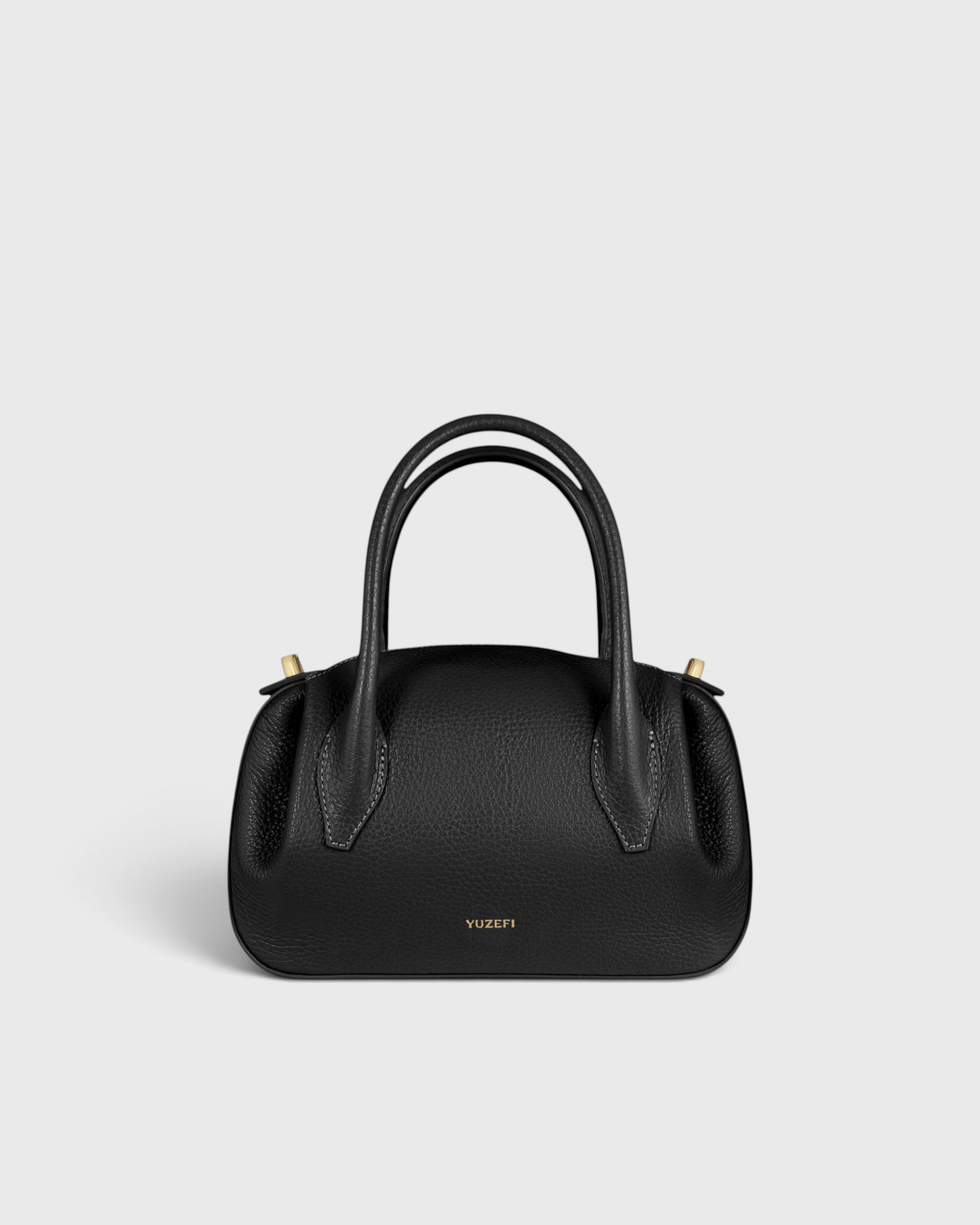 JONES + CO Oyster Mini Duffle in black pebble grained Italian leather with gold-tone hardware and top handles.