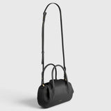 JONES + CO Oyster mini duffle bag in black pebble leather with gold hardware, top handles, and crossbody strap.