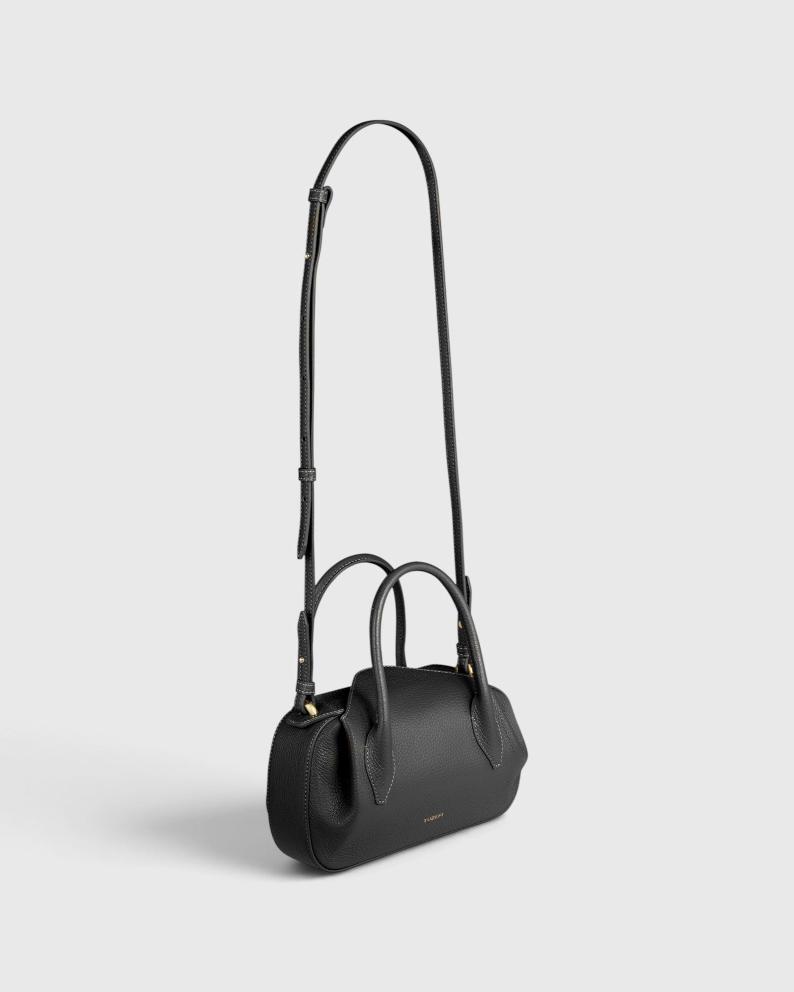 JONES + CO Oyster mini duffle bag in black pebble leather with gold hardware, top handles, and crossbody strap.