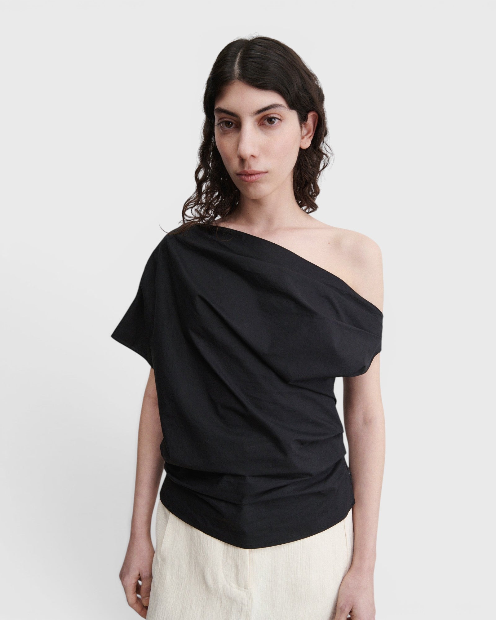 JONES + CO black one-shoulder blouse in organic crisp cotton with an asymmetric neckline and draped silhouette.