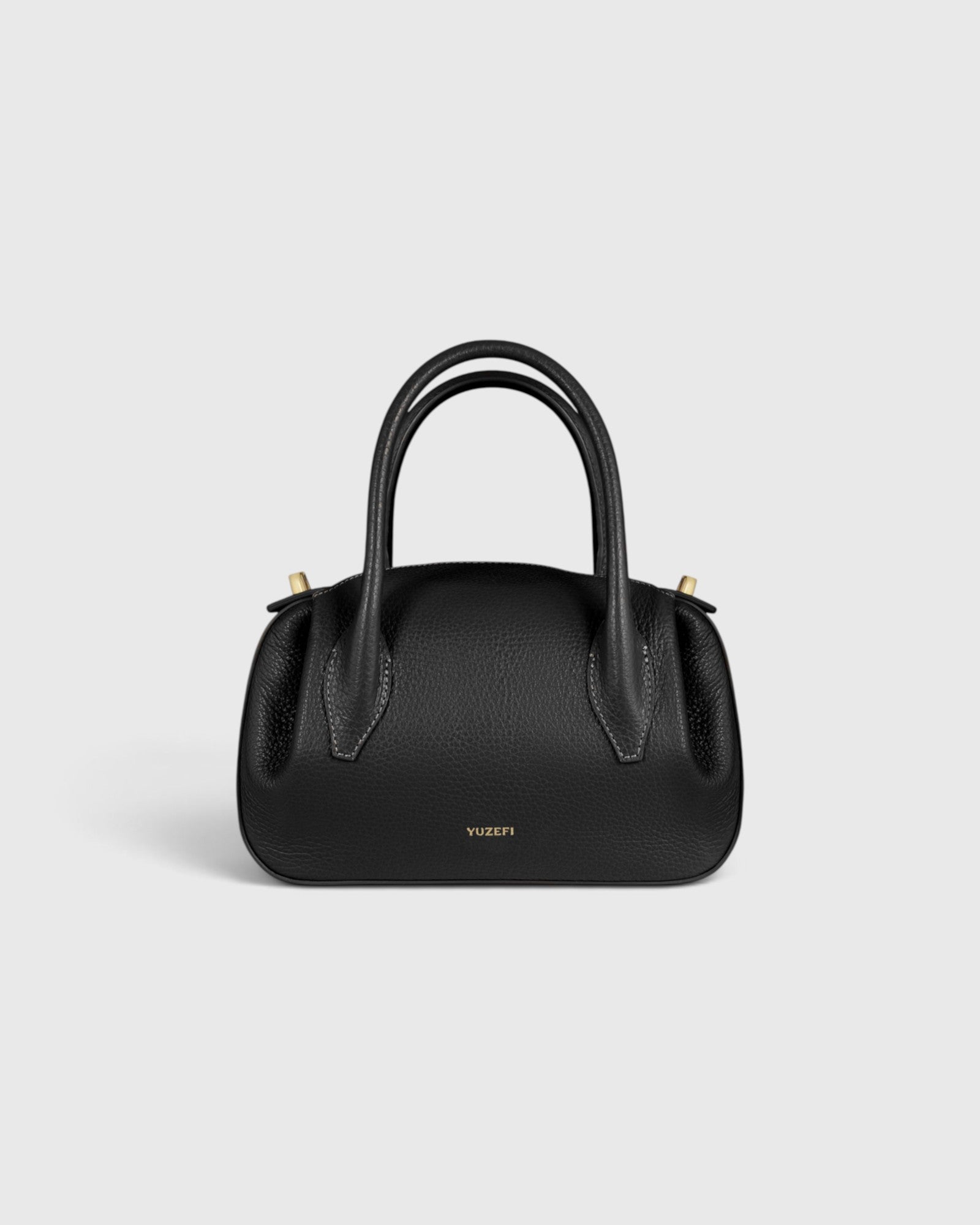 JONES + CO Oyster mini duffle bag in black pebble grained leather with gold-tone hardware and structured top handles.