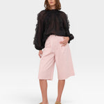 JONES + CO black sheer blouse with ruffled high neckline and voluminous sleeves. Model wears pink culottes.