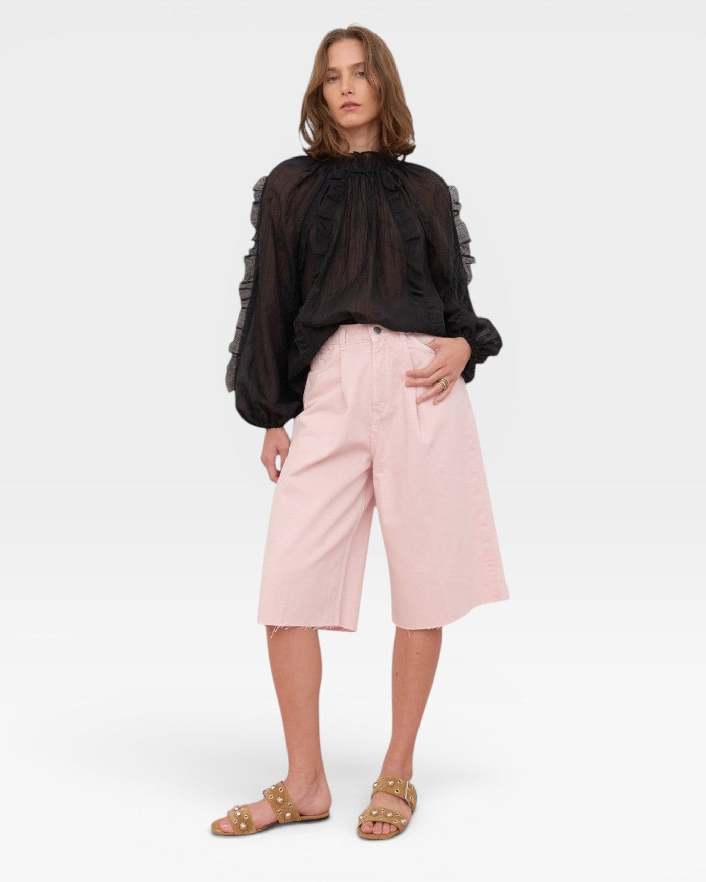 JONES + CO black sheer blouse with ruffled high neckline and voluminous sleeves. Model wears pink culottes.