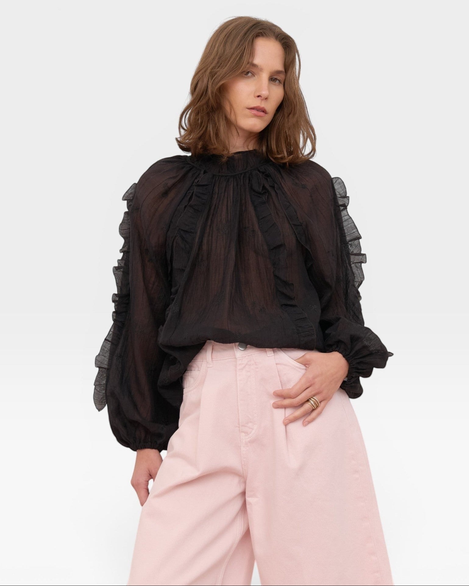 JONES + CO black sheer blouse with ruffled high neckline and voluminous sleeves, paired with pink wide-leg pants.