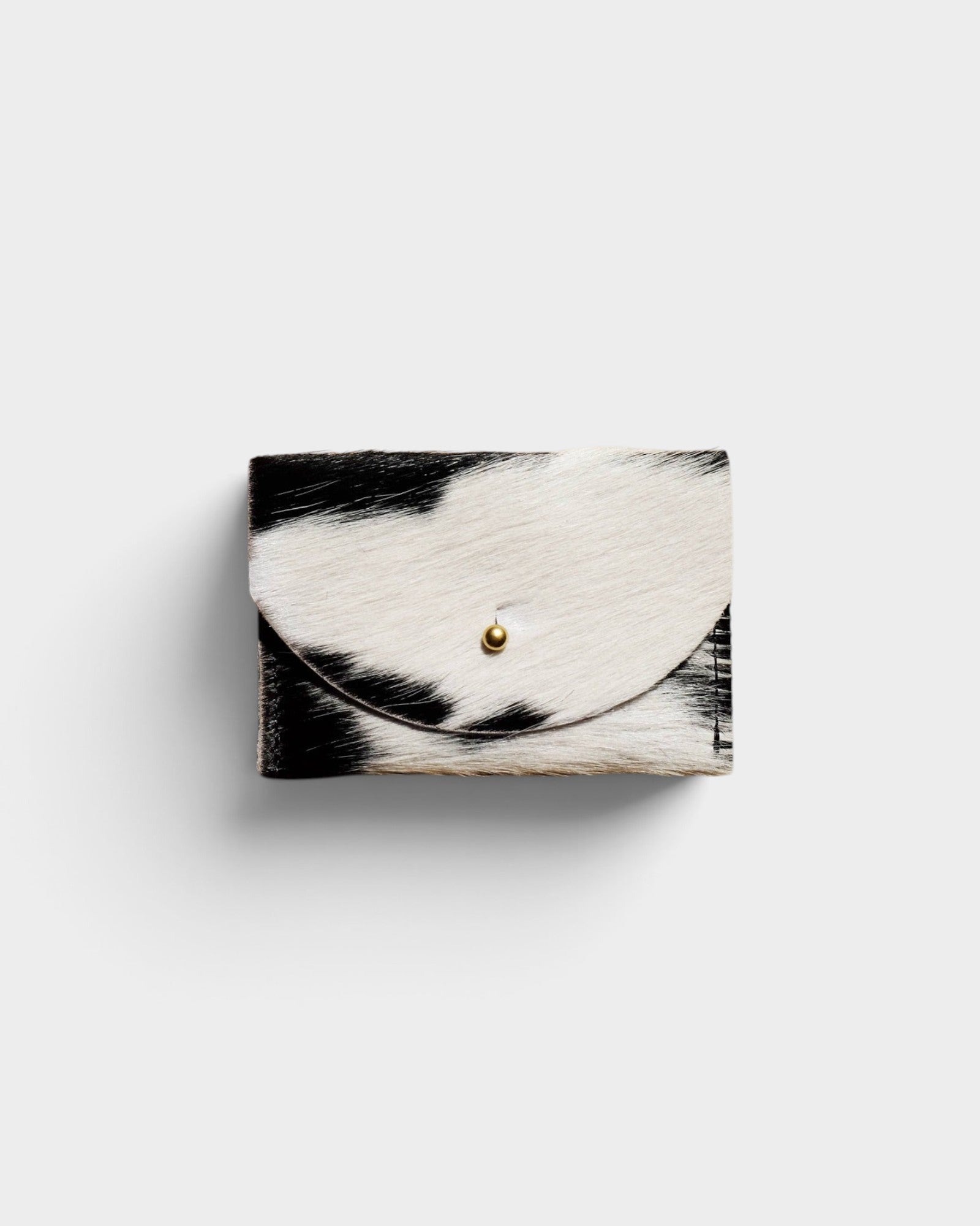 JONES + CO black and white cowhide cardholder with a solid brass fastener, featuring a natural hair-on-hide texture.