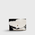 JONES + CO black and white cowhide cardholder with a solid brass fastener, featuring a natural hair-on-hide texture.